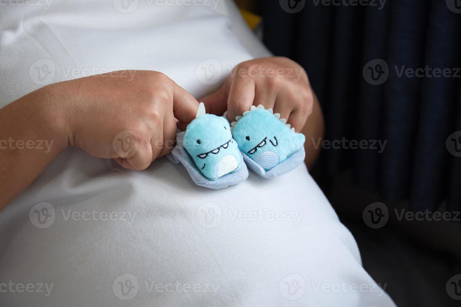 Young Happy Asian Pregnant holding small shoes for the unborn baby in her hand and look into the camera photo