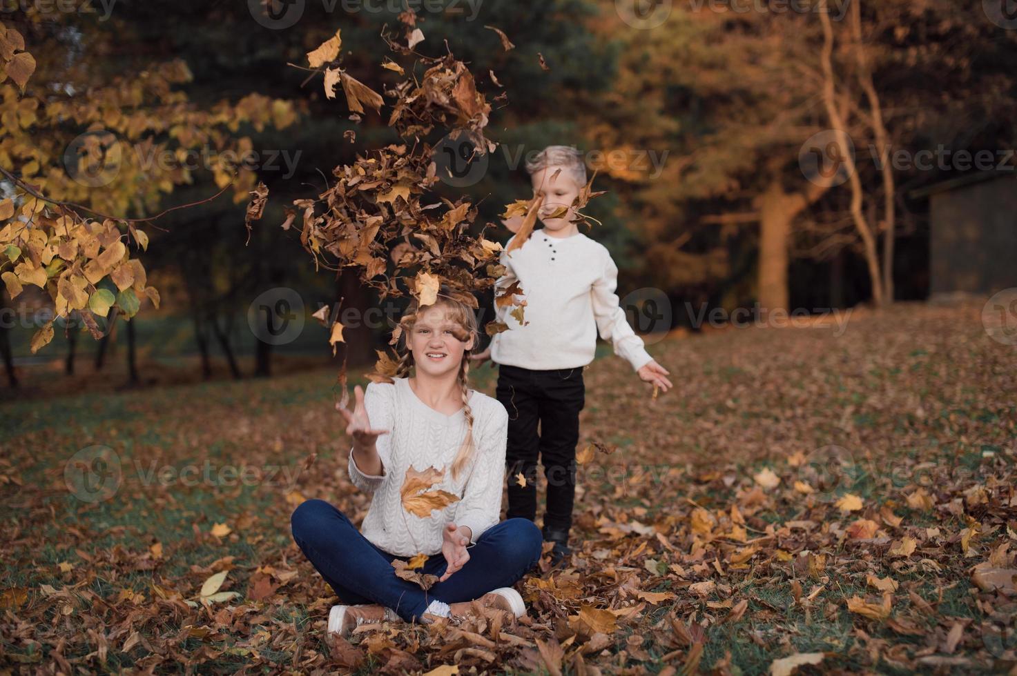 Happy girl and boy toss yellow autumn leaves in the forest photo