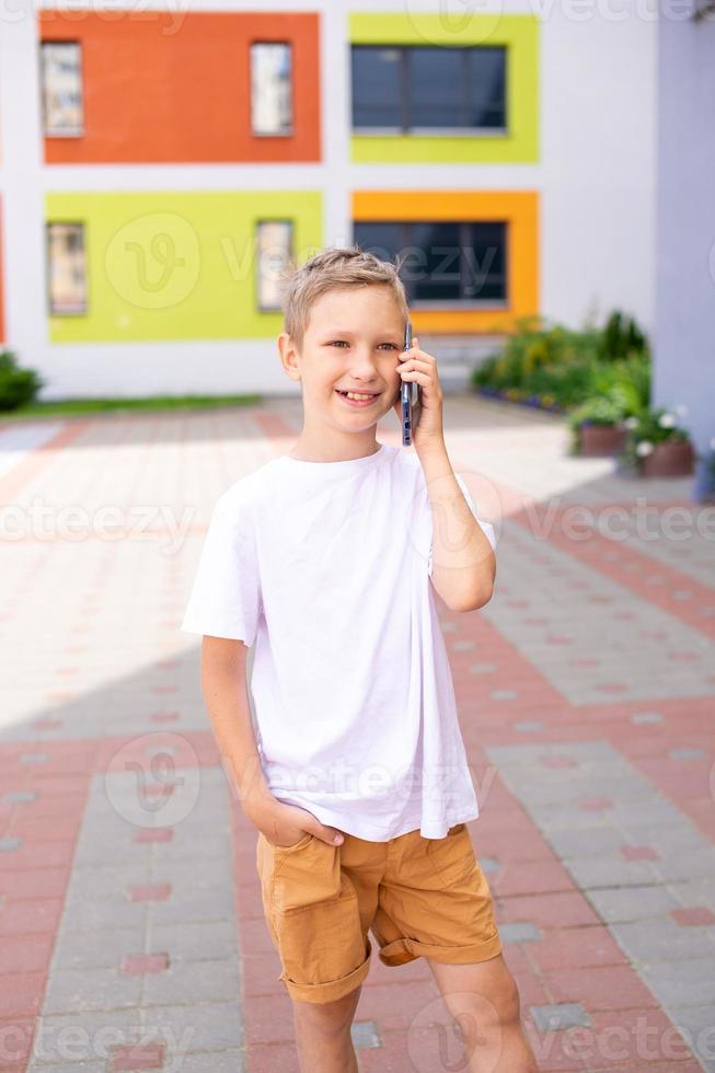 The boy is standing near the school talking on the phone photo