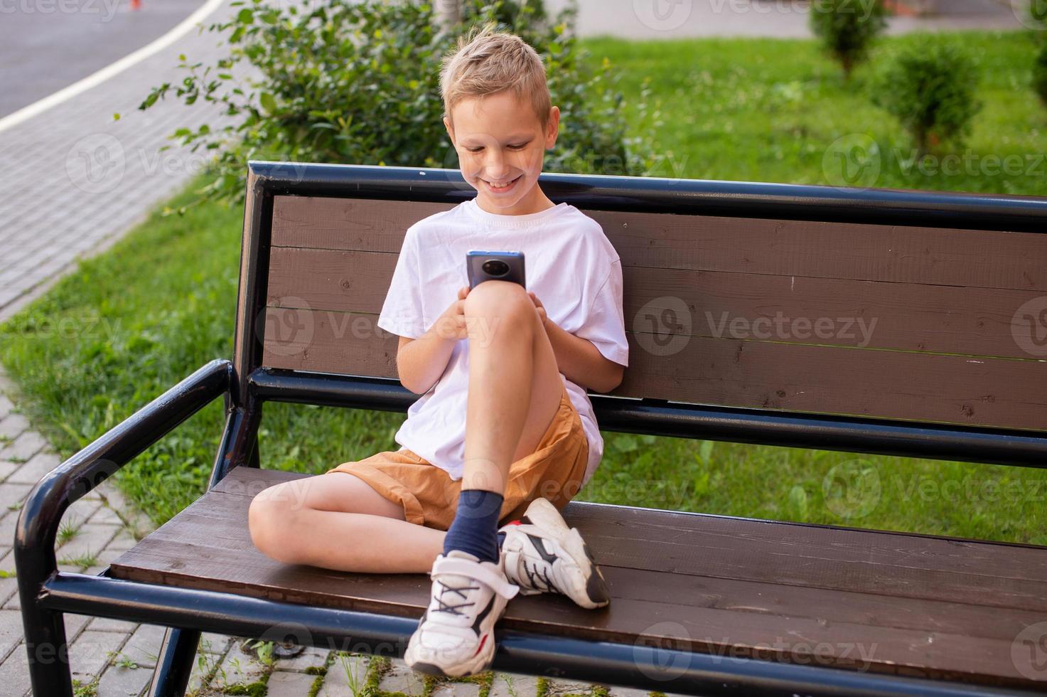 The boy is sitting on a bench and looking at the phone photo