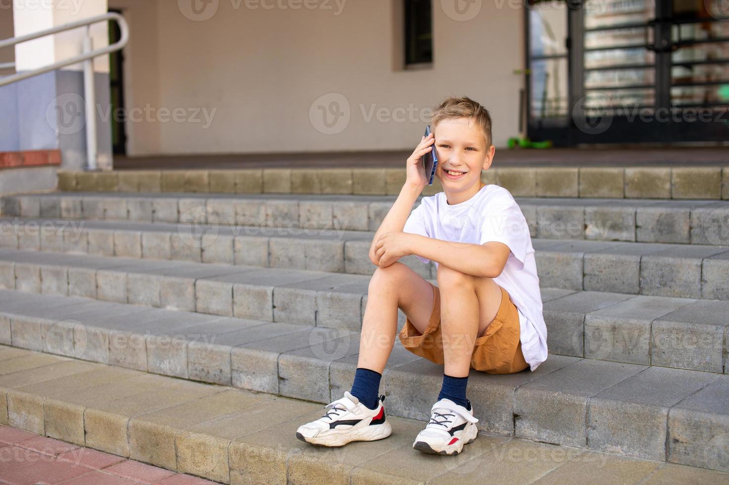 The boy is sitting on the steps and talking on the phone photo