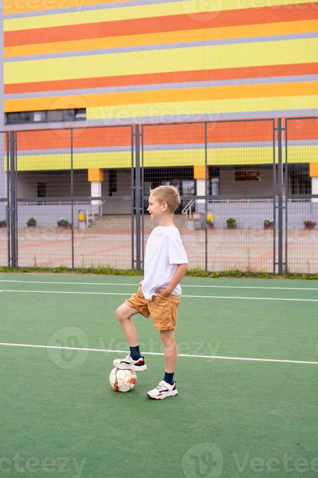 A teenage boy stands on a green field in the school yard with a soccer ball photo