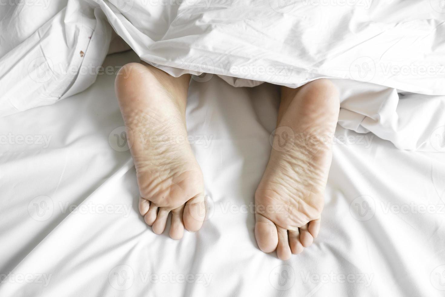 Couple feet under sheets on the bed at home. photo
