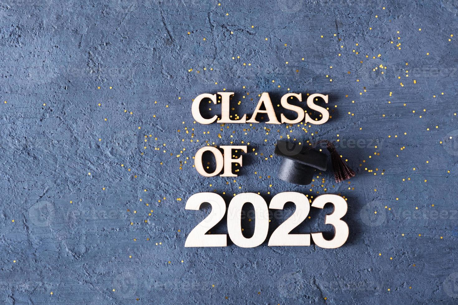 Class of 2023 concept. Wooden number 2023 with graduated cap on dark concrete background with tinsel photo