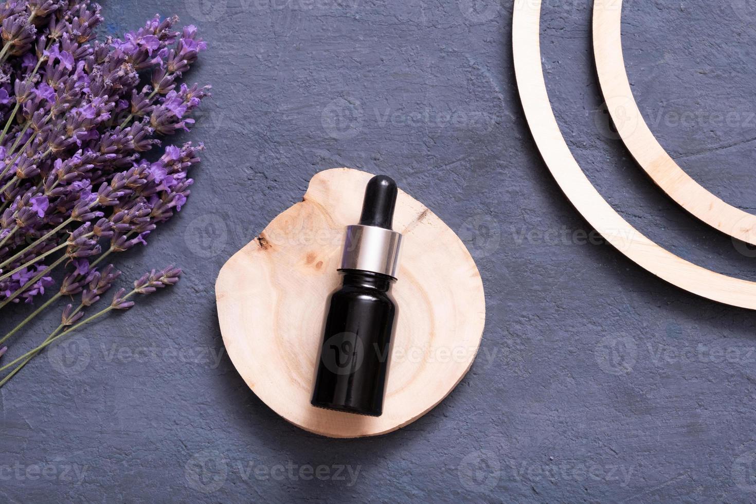 Dropper bottle with lavender flowers and wooden podium on dark background. Wellness flat lay concept. photo