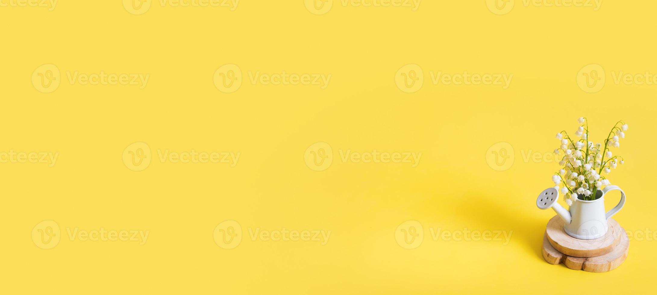 Banner with lilies of the valley bouquet in a decorative watering can on a yellow background with copy space photo