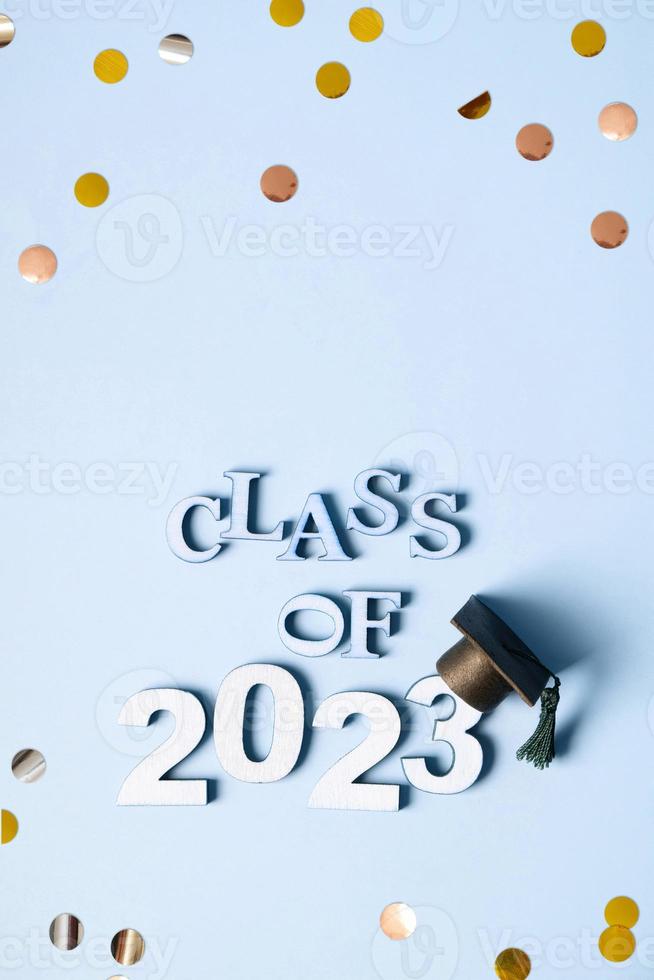 Class of 2023 concept. Wooden number 2023 with graduated cap on blue background with tinsel top view photo