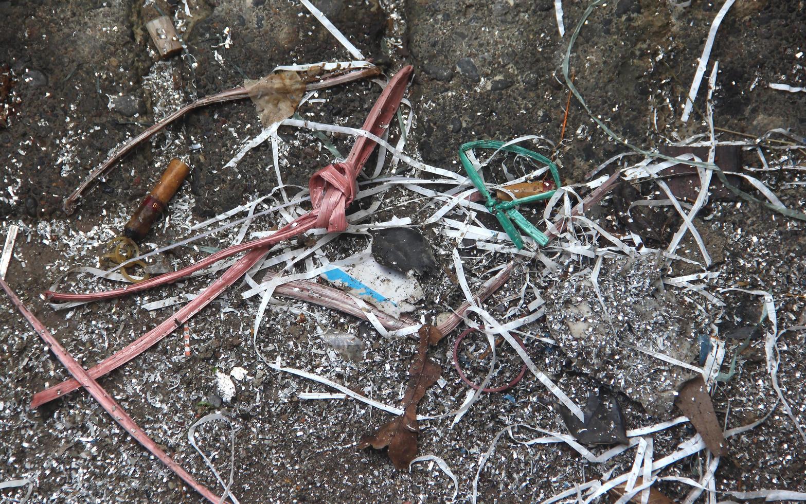 Dirty and messy dark gray asphalt textured background with tali rafia thread, dried leaves, cigarette waste, shredded white paper, and other industrial waste. photo