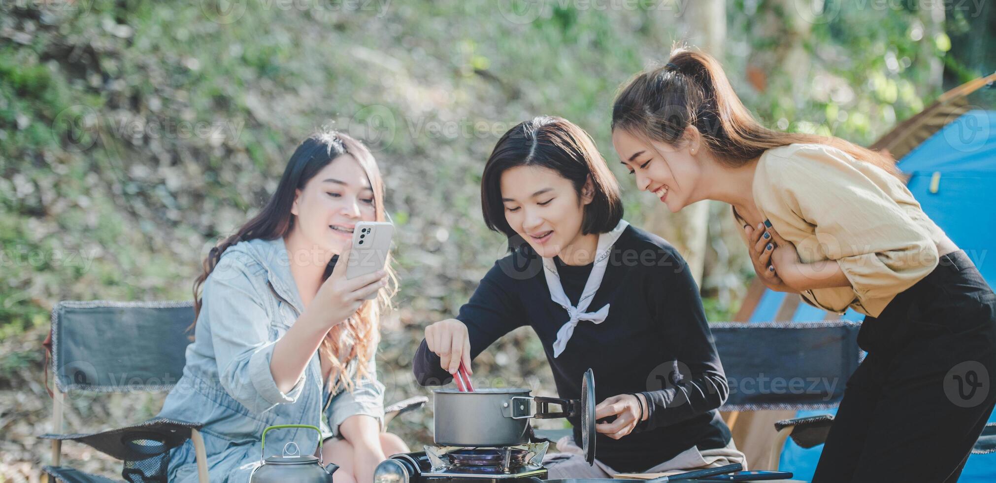 las mujeres jóvenes cocinan y usan el teléfono inteligente toman fotos en el campamento