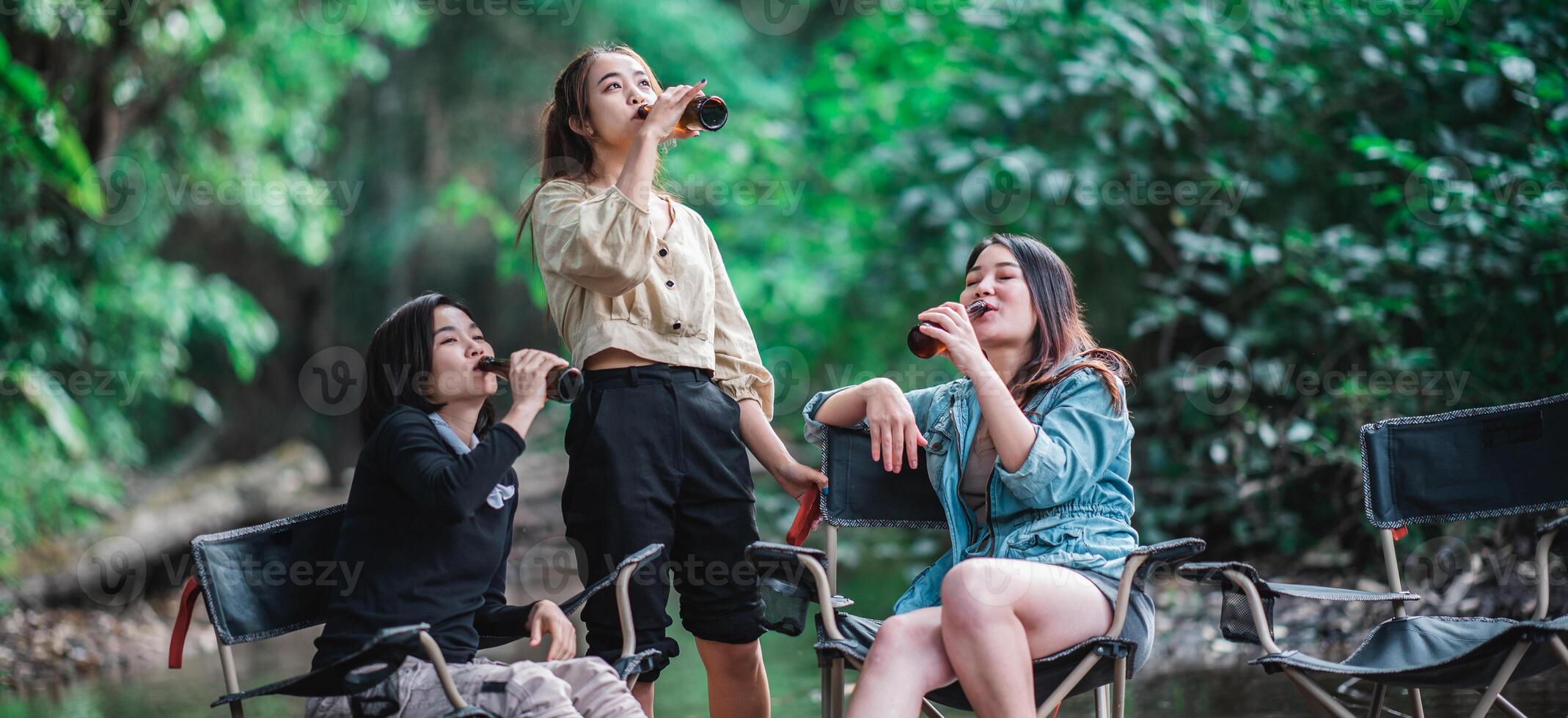 Young women sitting and drink beverage  while camping in forest photo