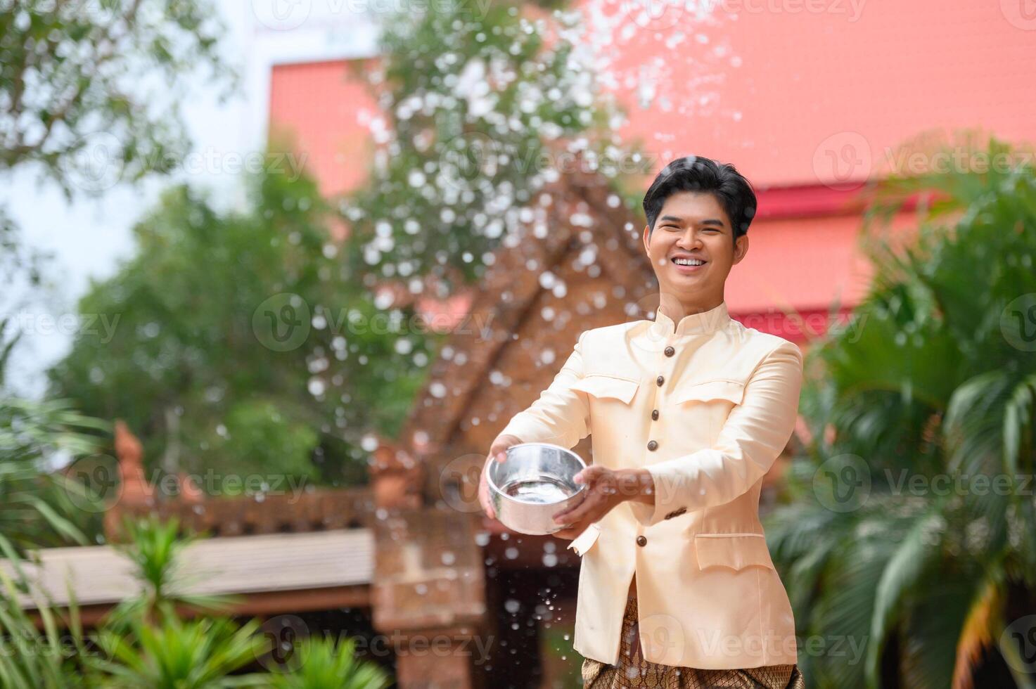 Young man splashing water from bowl on Songkran festival photo
