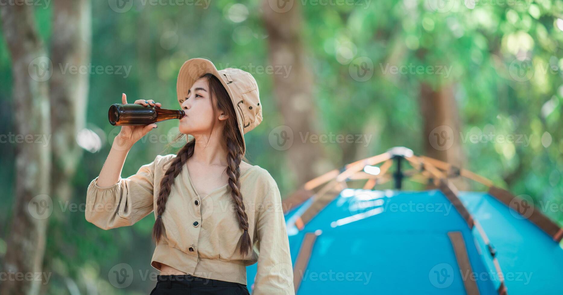 Young woman cheer and drink beverage  front of camping tent photo