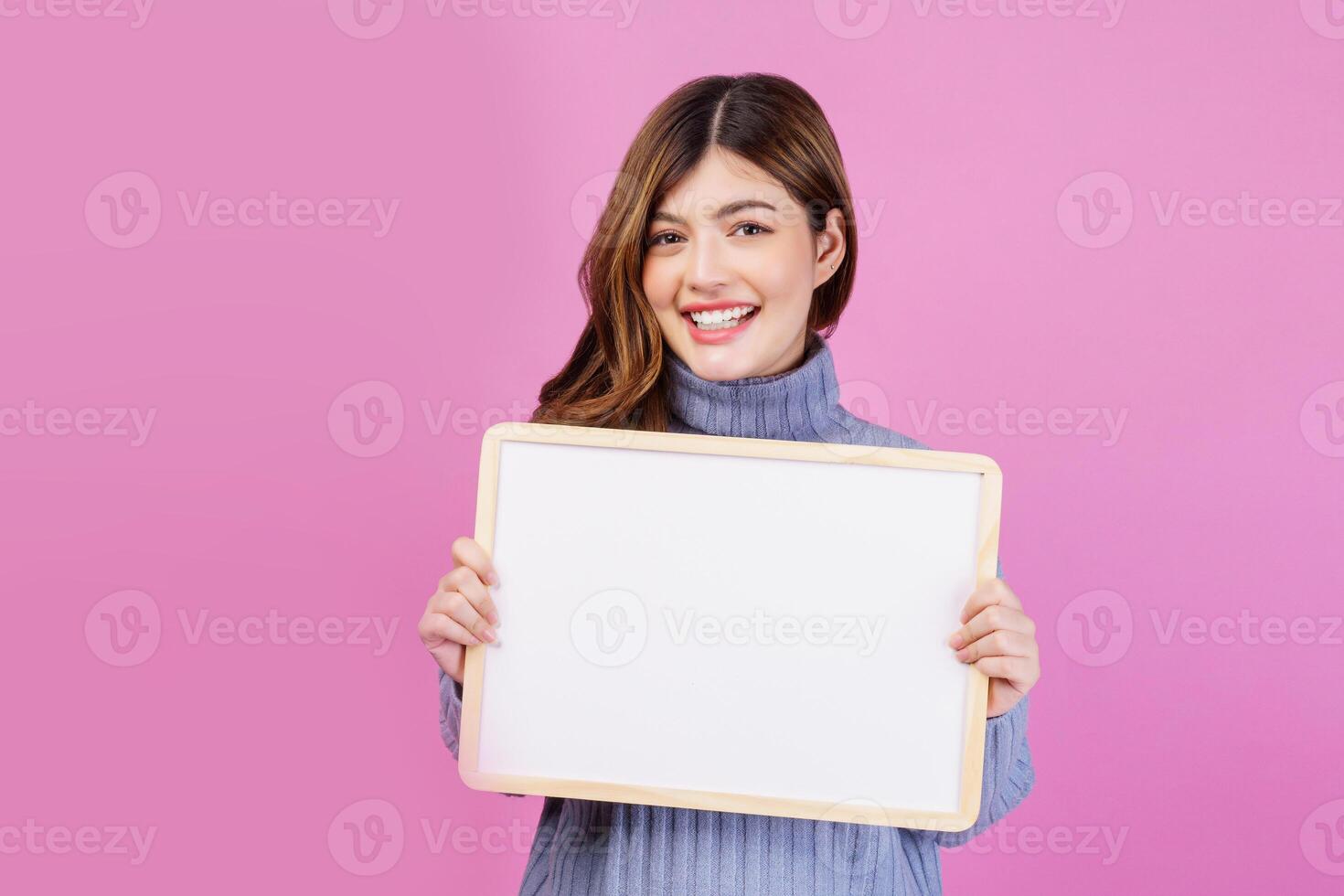 Portrait of Happy young woman holding an empty white placard over isolated pink background. photo