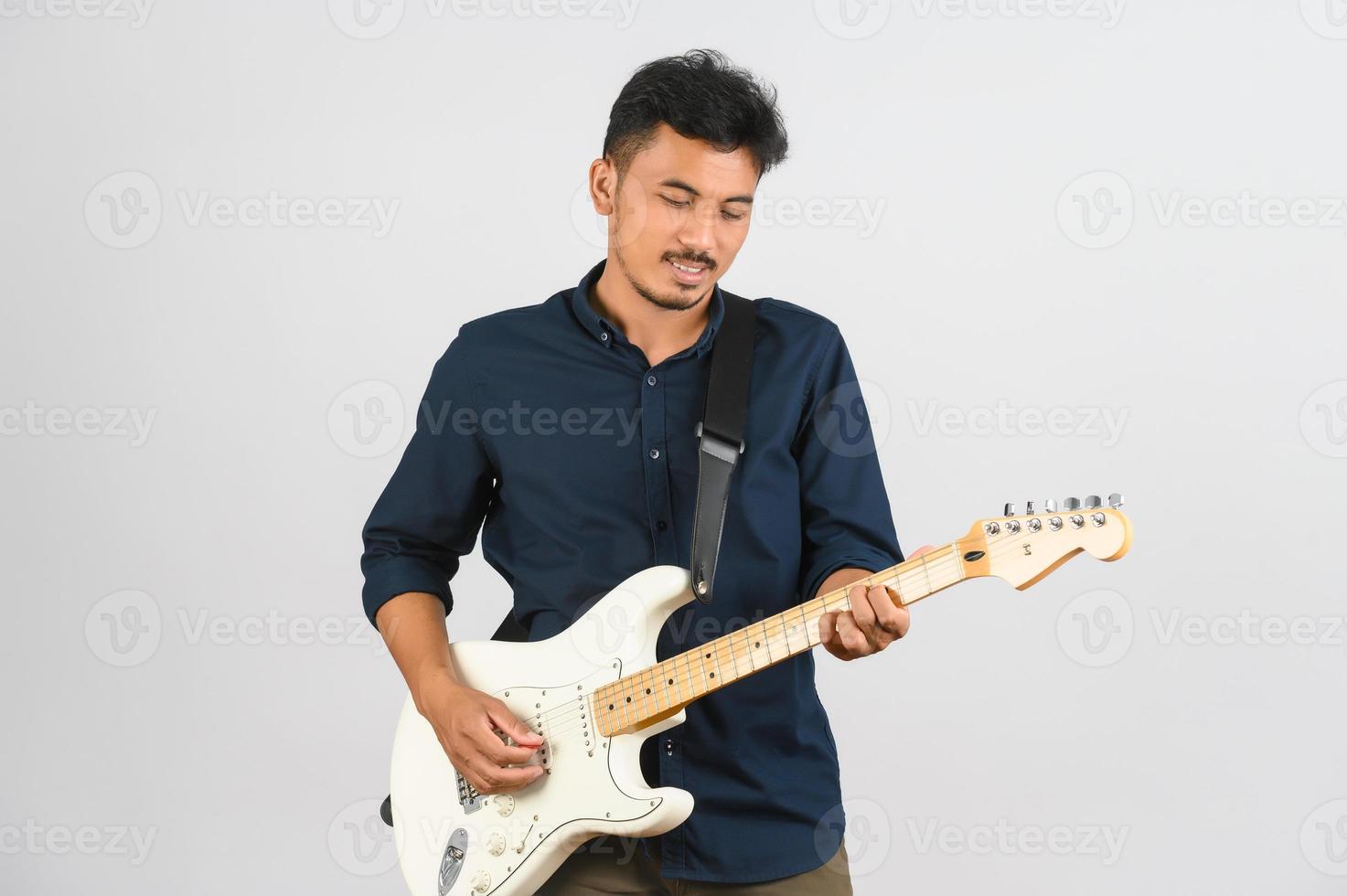 retrato de un joven asiático con camisa azul y guitarra electrónica aislado de fondo blanco foto