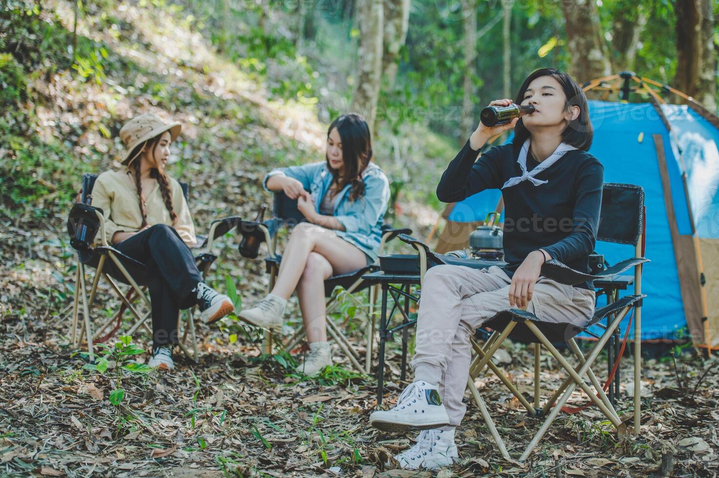 Young women sitting and drink beverage  front of camping tent photo