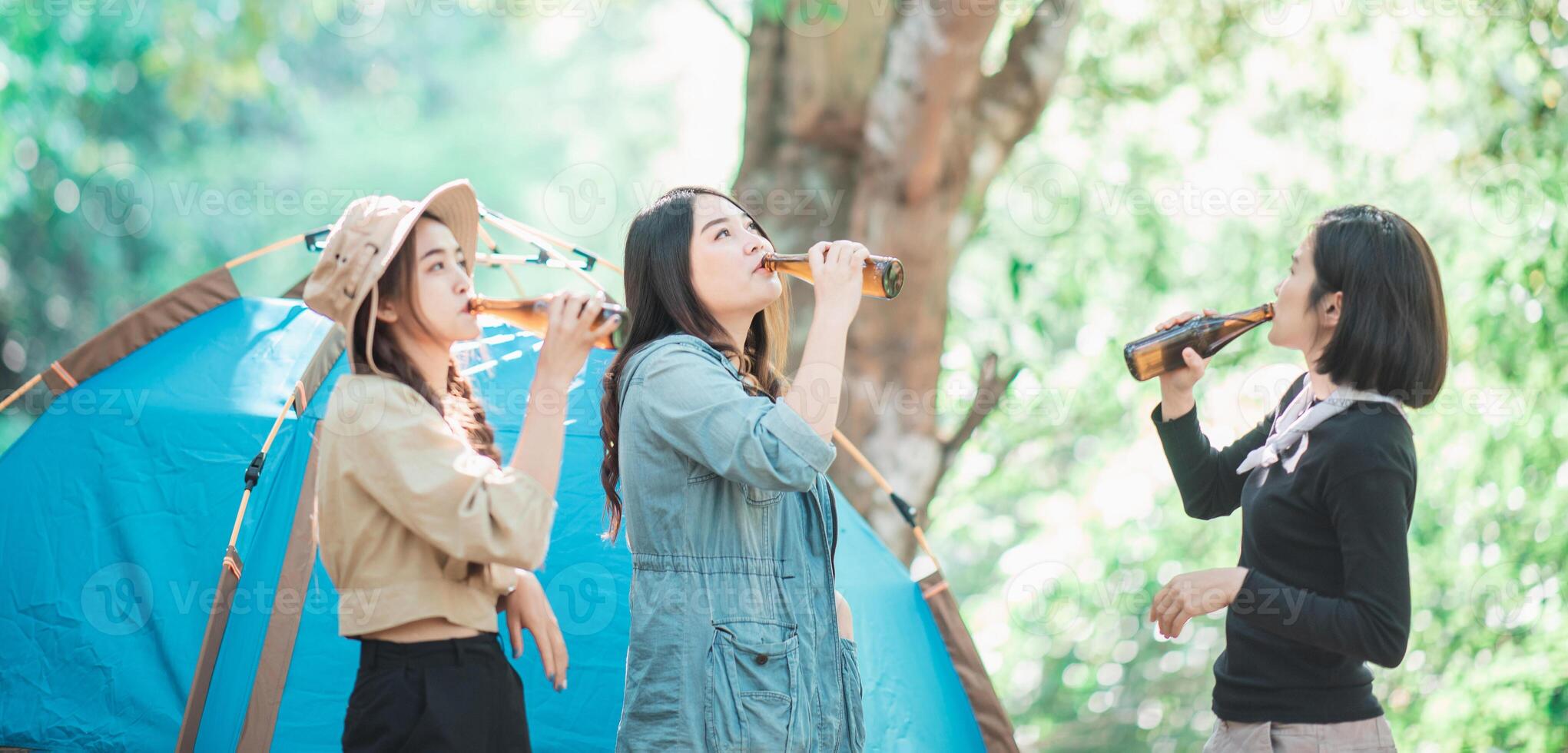 Young women cheer and drink beverage  front of camping tent photo