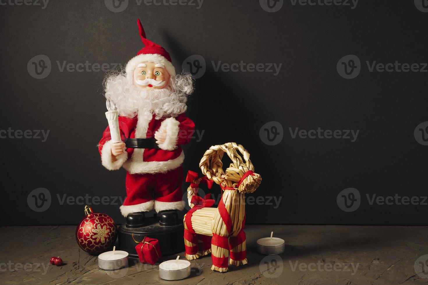 Santa Claus doll in a red suit with a candle, gifts, a Christmas ball and a Christmas deer photo