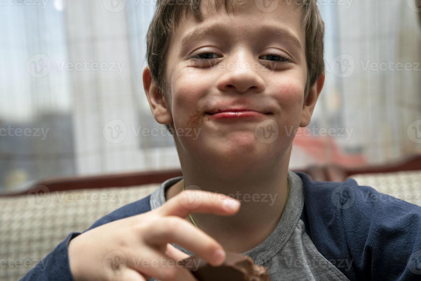 portrait of a funny cute Caucasian boy who eats chocolate sitting at a table in a home kitchen photo