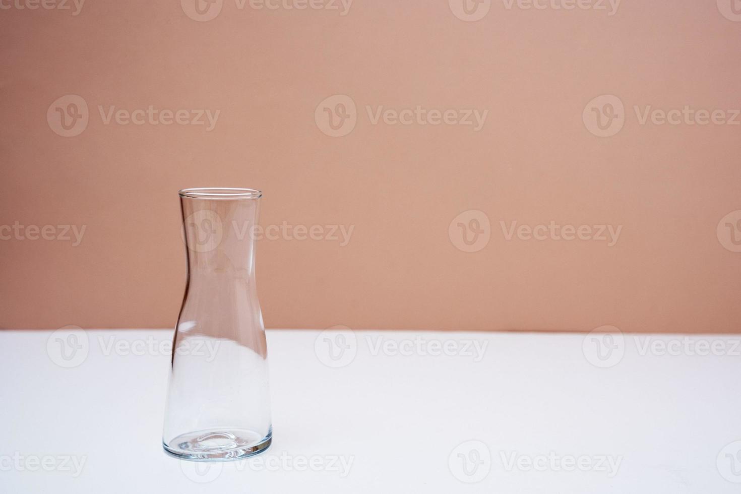 An empty glass vase on the table on a peach background photo