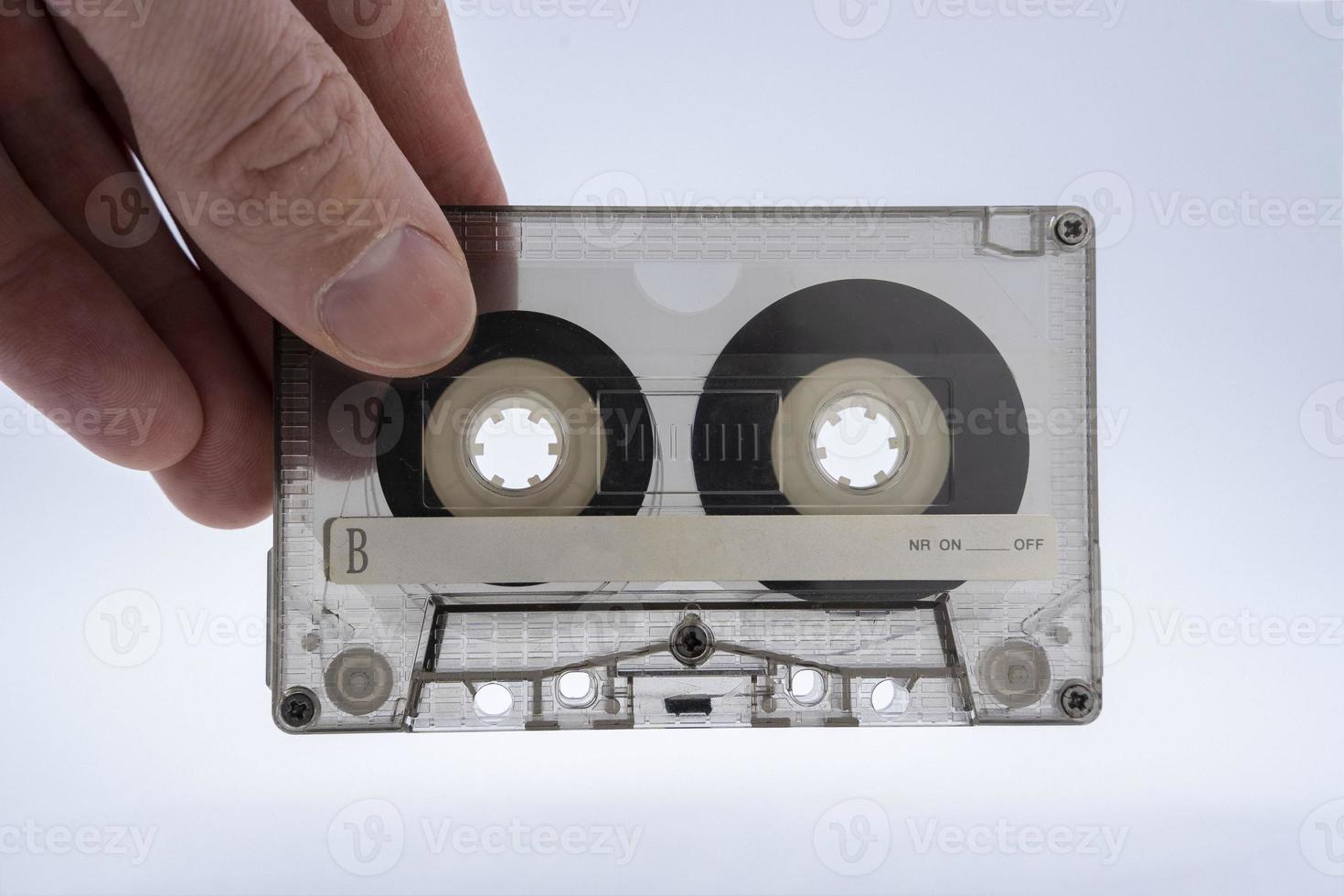 A man's hand holds an old stained glass transparent audio cassette for a tape recorder photo