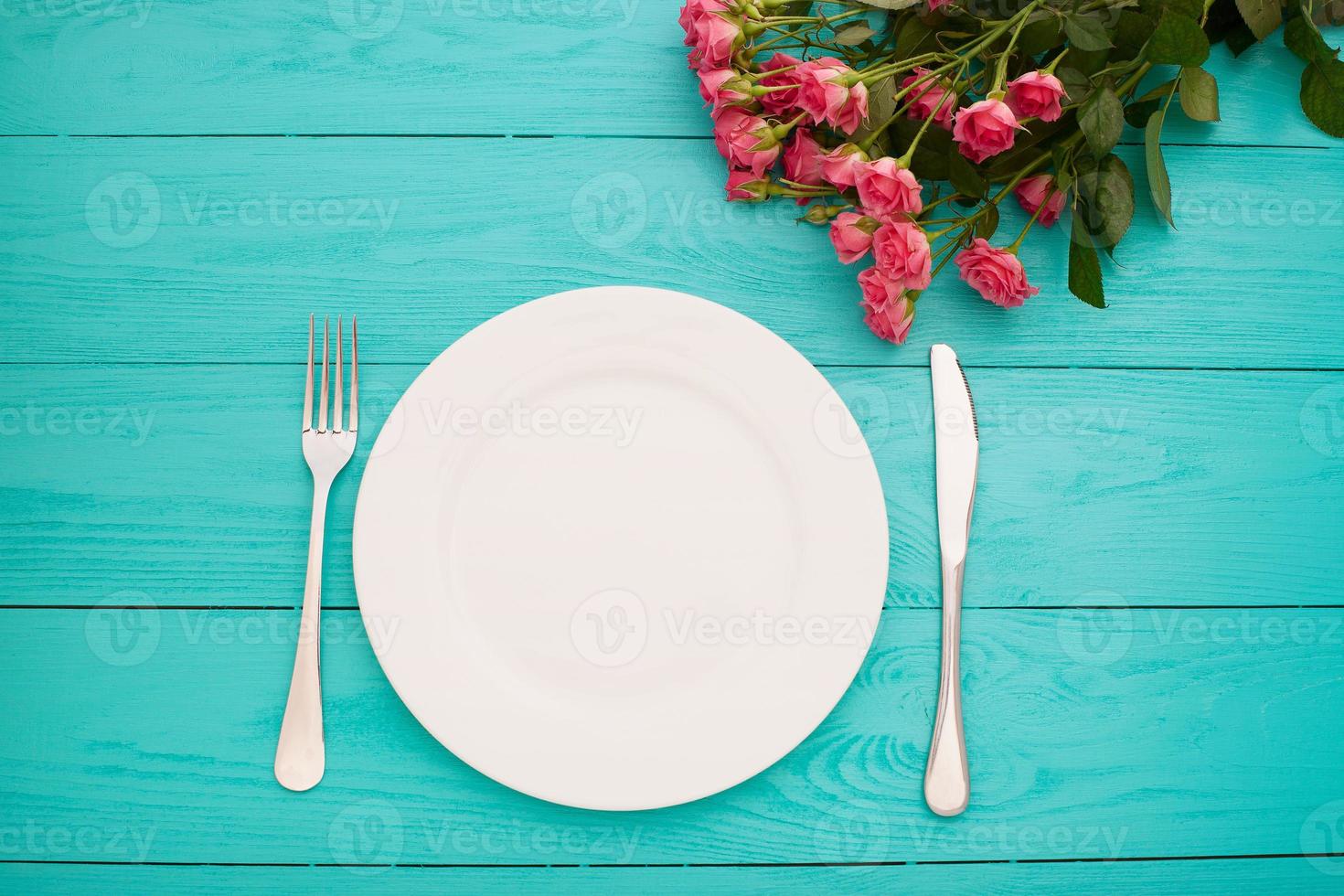 Top view of tableware of round and heart shaped empty plate, metal knife and fork served on white wooden table with glowing candle and gift box prepared for celebration of saint valentine day photo