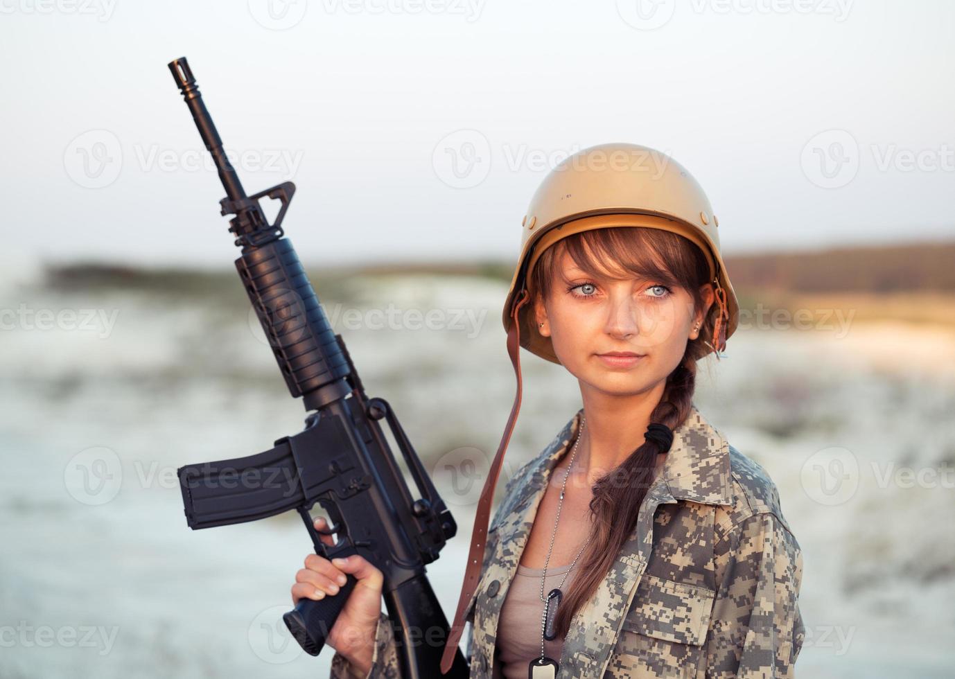 Young female soldier dressed in a camouflage with a gun in the outdoor photo