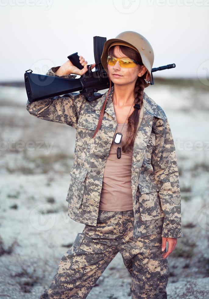 joven hembra soldado vestido en un camuflaje con un pistola en el al aire libre foto