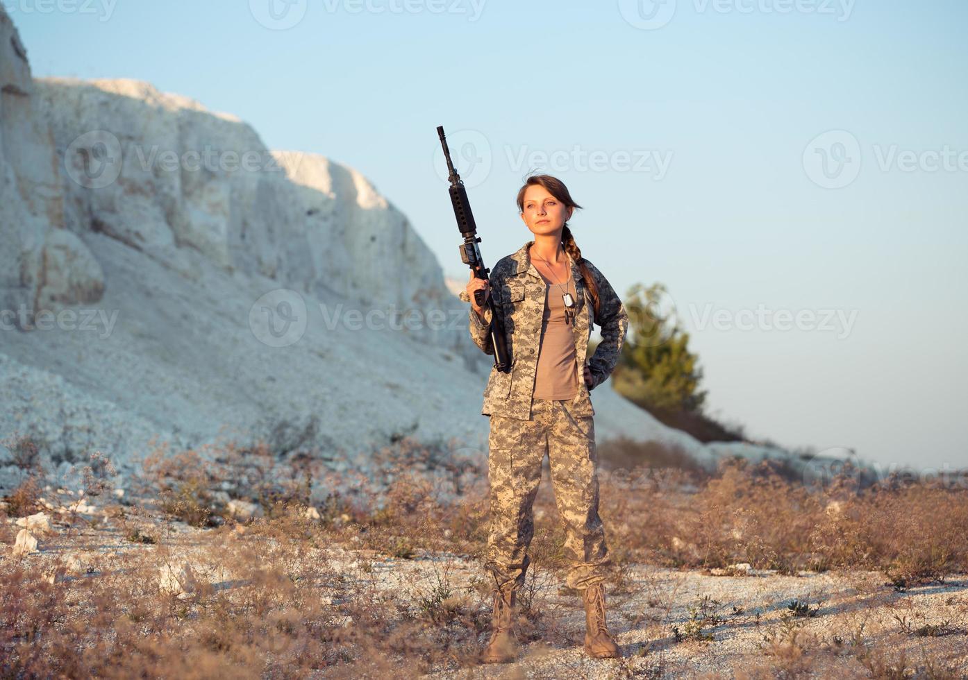 joven hembra soldado vestido en un camuflaje con un pistola en el ubicación foto