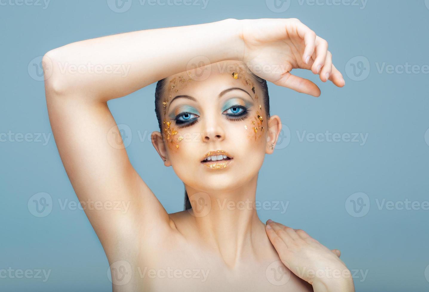Glamorous portrait of young beautiful girl with big blue eyes, lush lashes and bright golden makeup photo