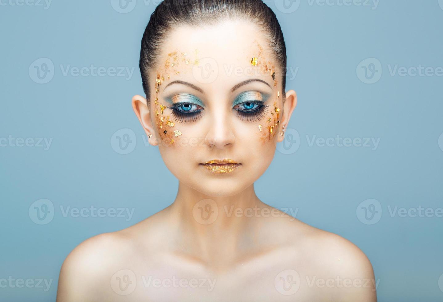 Glamorous portrait of young beautiful girl with big blue eyes, lush lashes and bright golden makeup photo