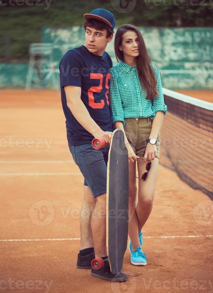 Young couple standing on a skateboard on the tennis court photo