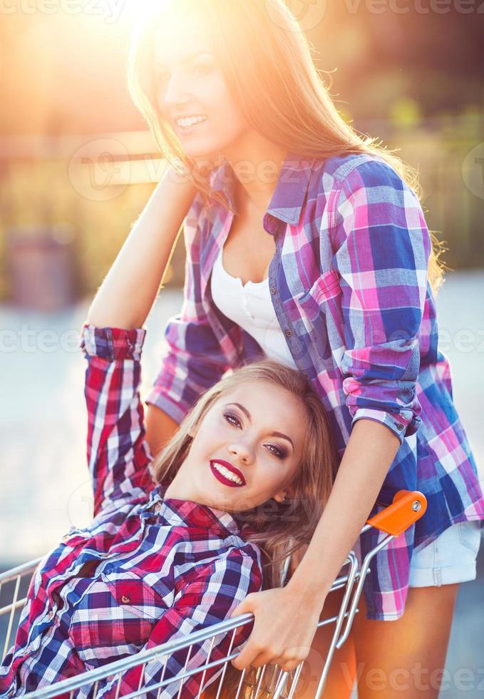 Two happy beautiful teen girls driving shopping cart outdoors photo