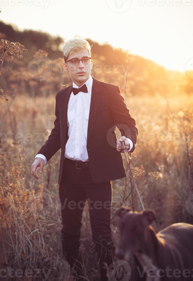 joven atractivo hombre en traje y Corbata con un galgo perro en otoño al aire libre foto