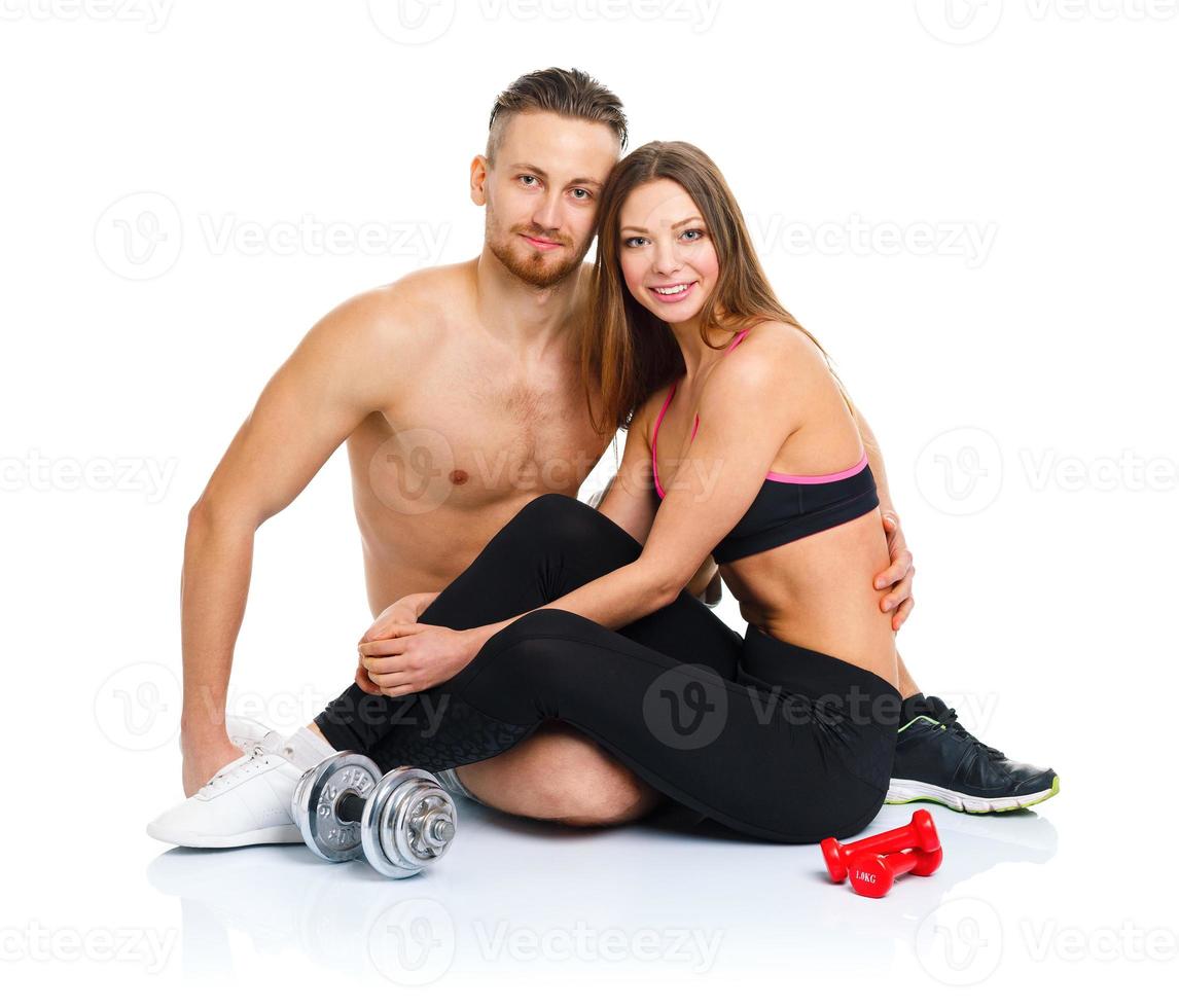 Athletic couple - man and woman after fitness exercise sitting with dumbbells on the white photo