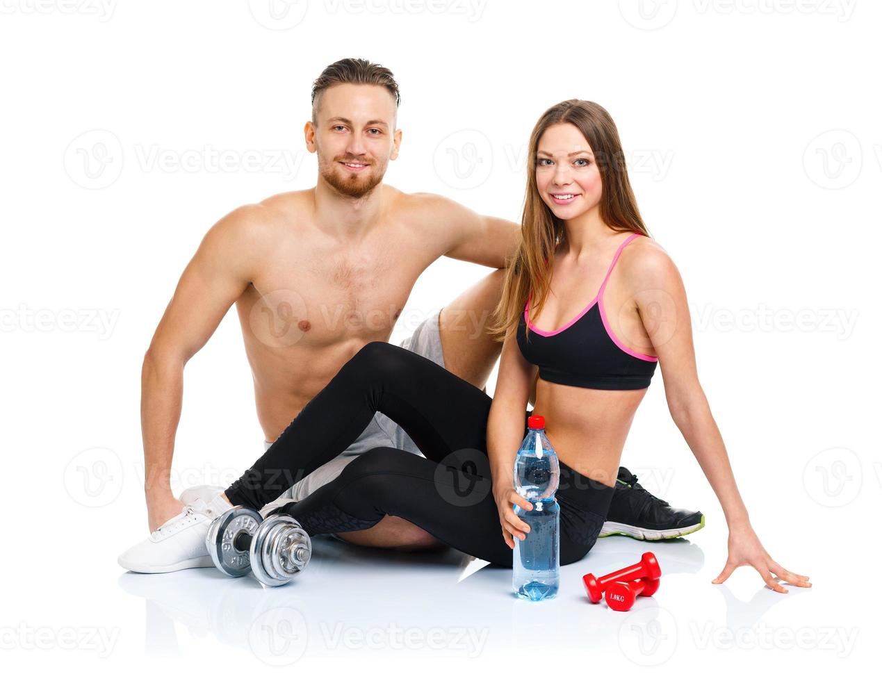 Athletic couple - man and woman after fitness exercise sitting with dumbbells on the white photo