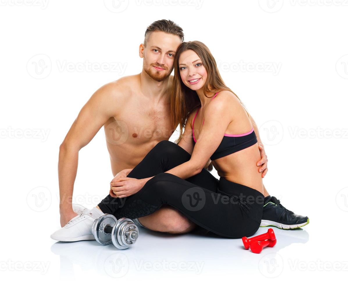 Sport couple - man and woman after fitness exercise sitting with dumbbells on the white photo