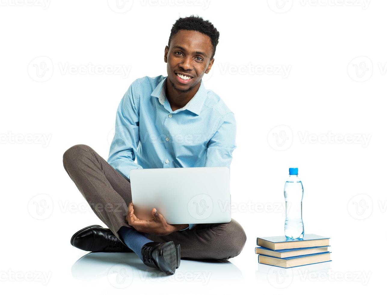 Happy african american college student with laptop, books and bottle of water sitting on white photo