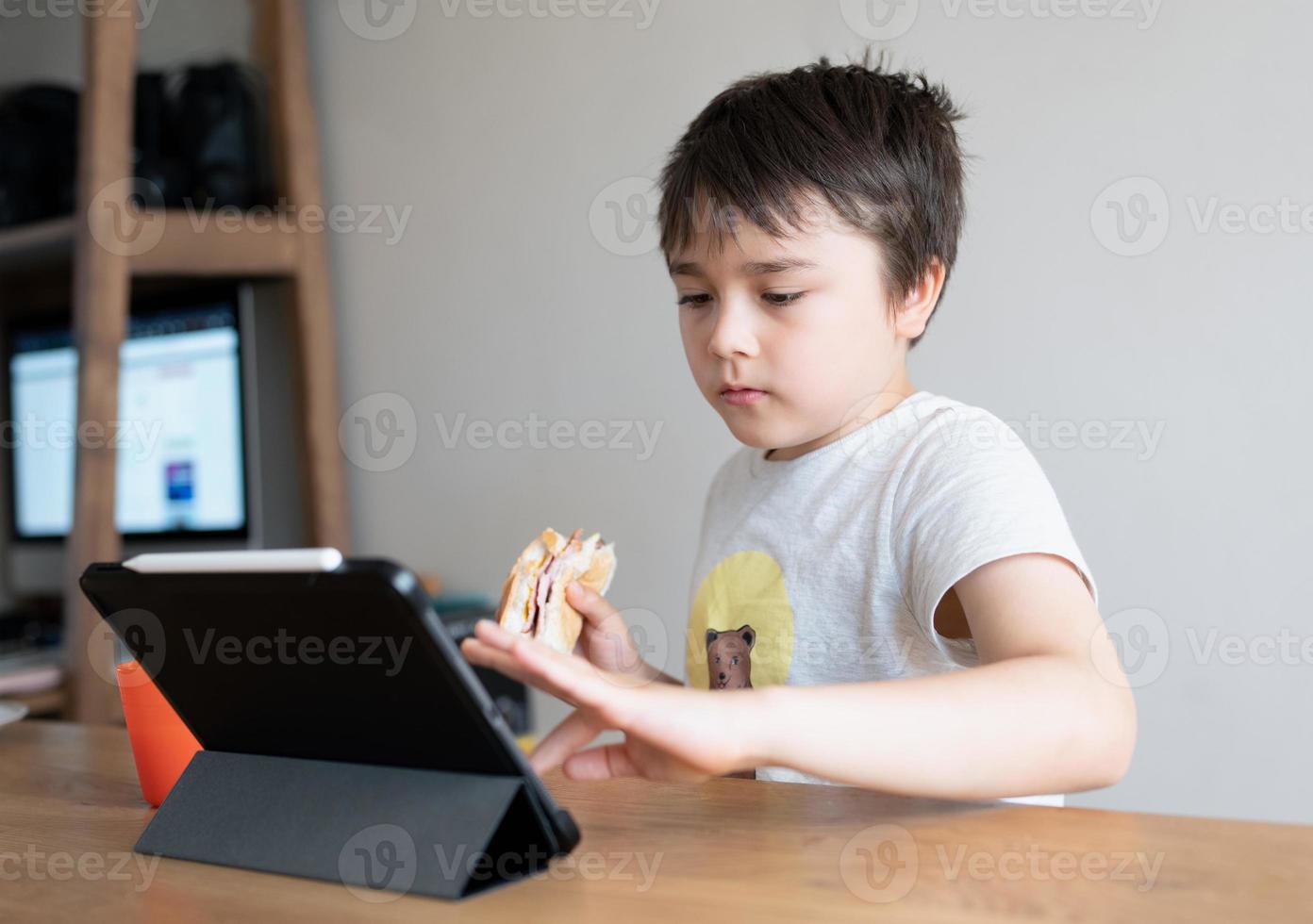 Kid eating eating homemade bacon sandwiches and watching cartoon on tablet, Child boy having  breakfast and playing game online on internet with friends before go to school in the morning photo