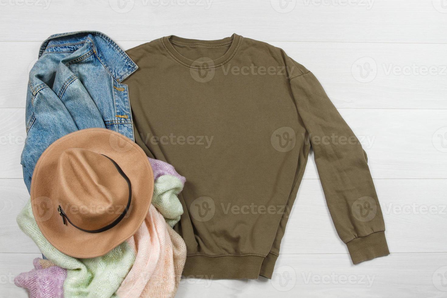 Sweatshirt mockup. Template blank khaki shirt top view on white wooden background. Winter outfit on wood floor. Woman fashion clothes. Spring look of today. Female Jeans, hat, scarf accessories photo