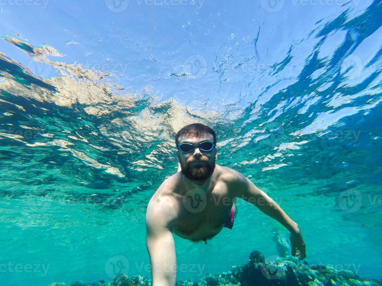 Young bearded man diving in a blue clean water photo