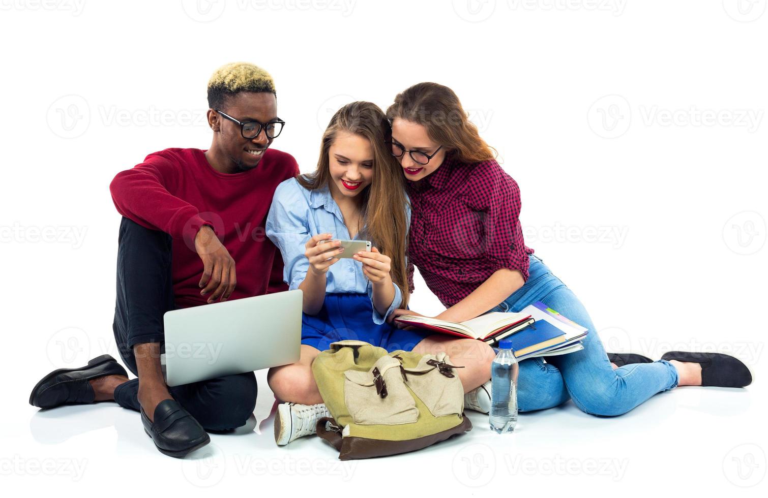 Tres contento estudiantes sentado con libros, ordenador portátil y pantalones foto