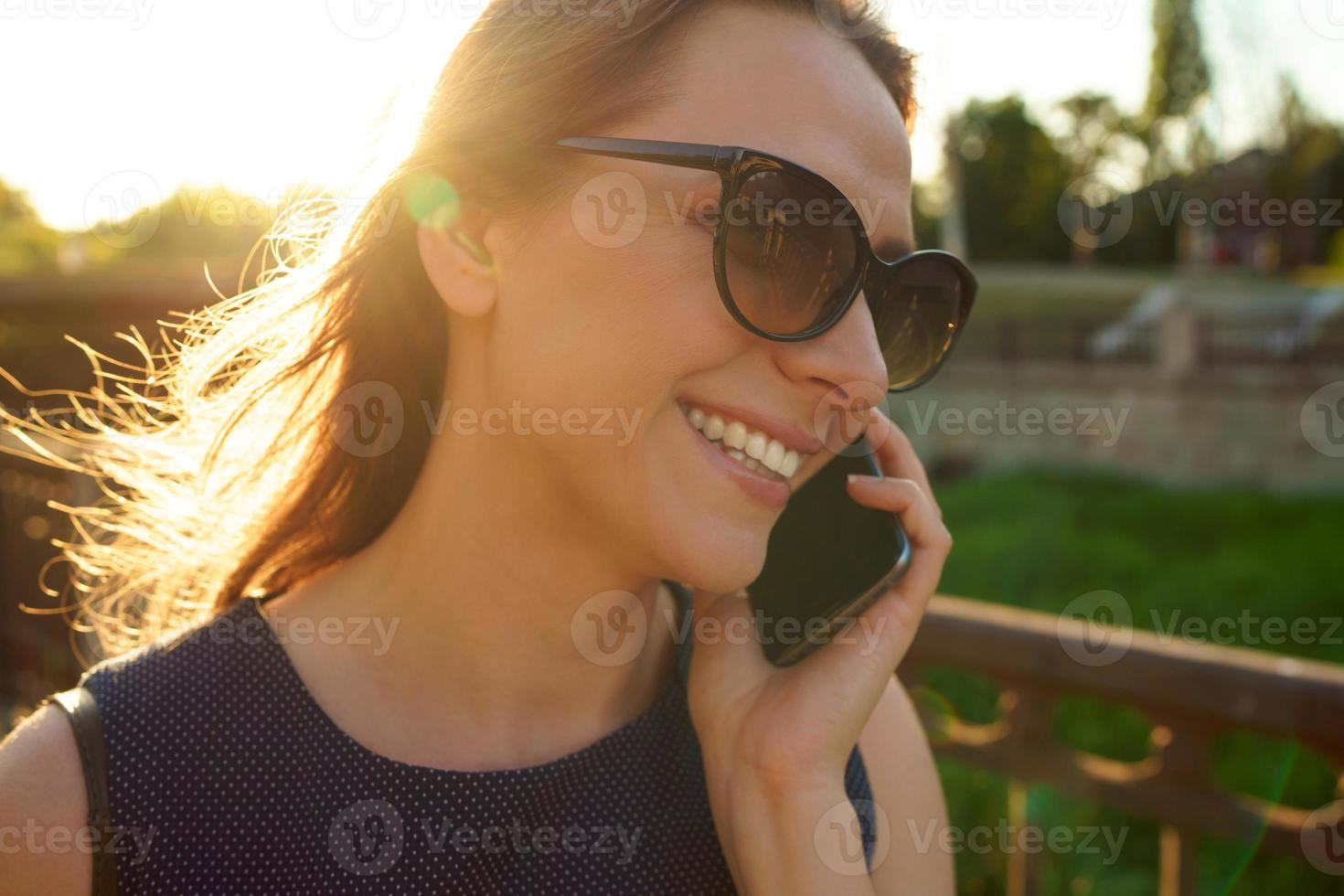Woman in sunglasses talking on the smartphone while walking down the street at sunset, close up photo
