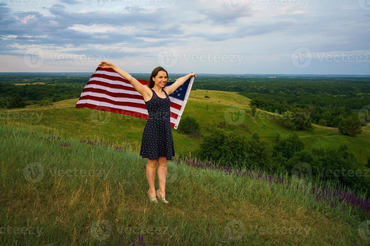 orgulloso mujer con un nosotros bandera es en pie en parte superior de un colina foto