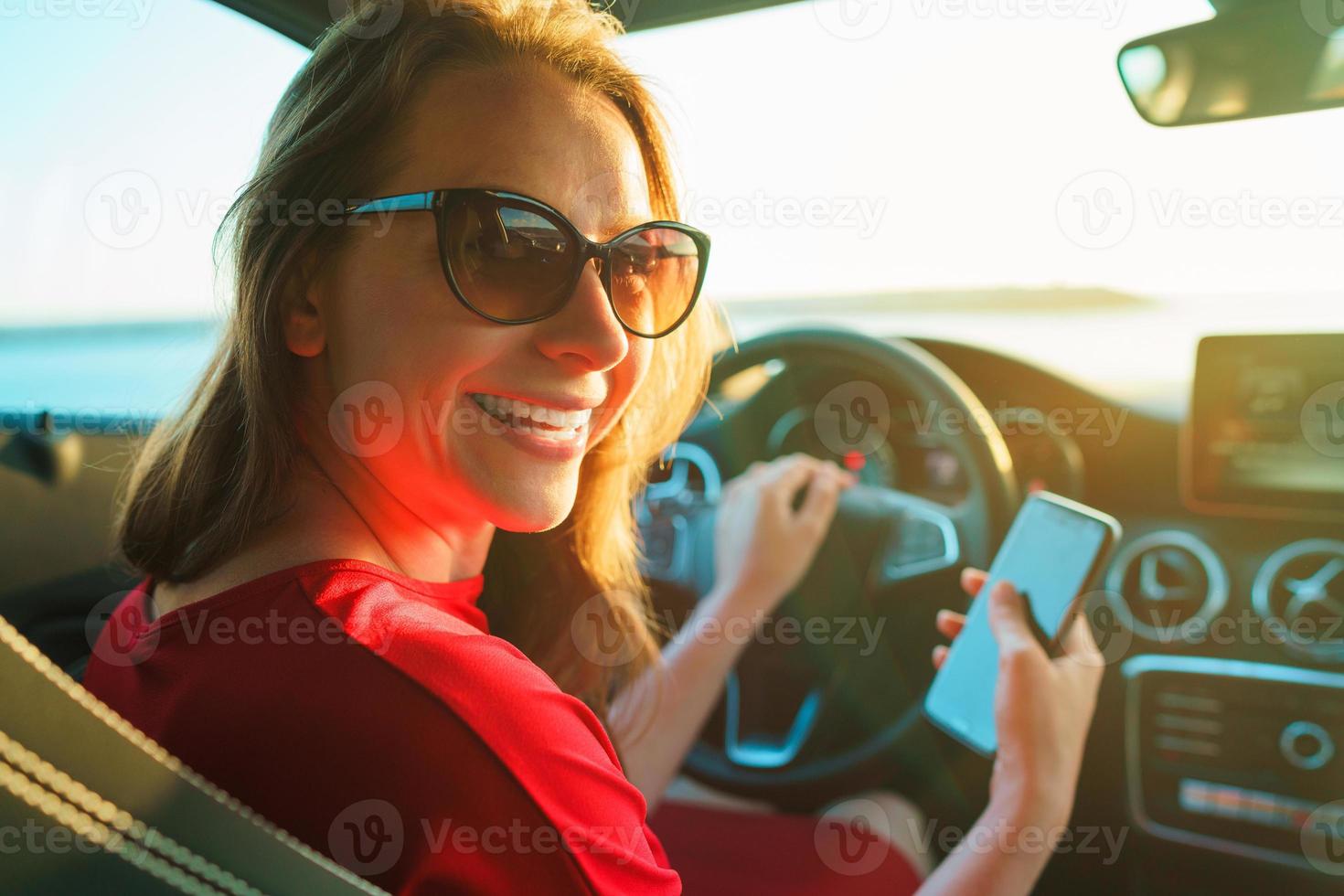 Happy woman uses a smartphone while driving a car photo