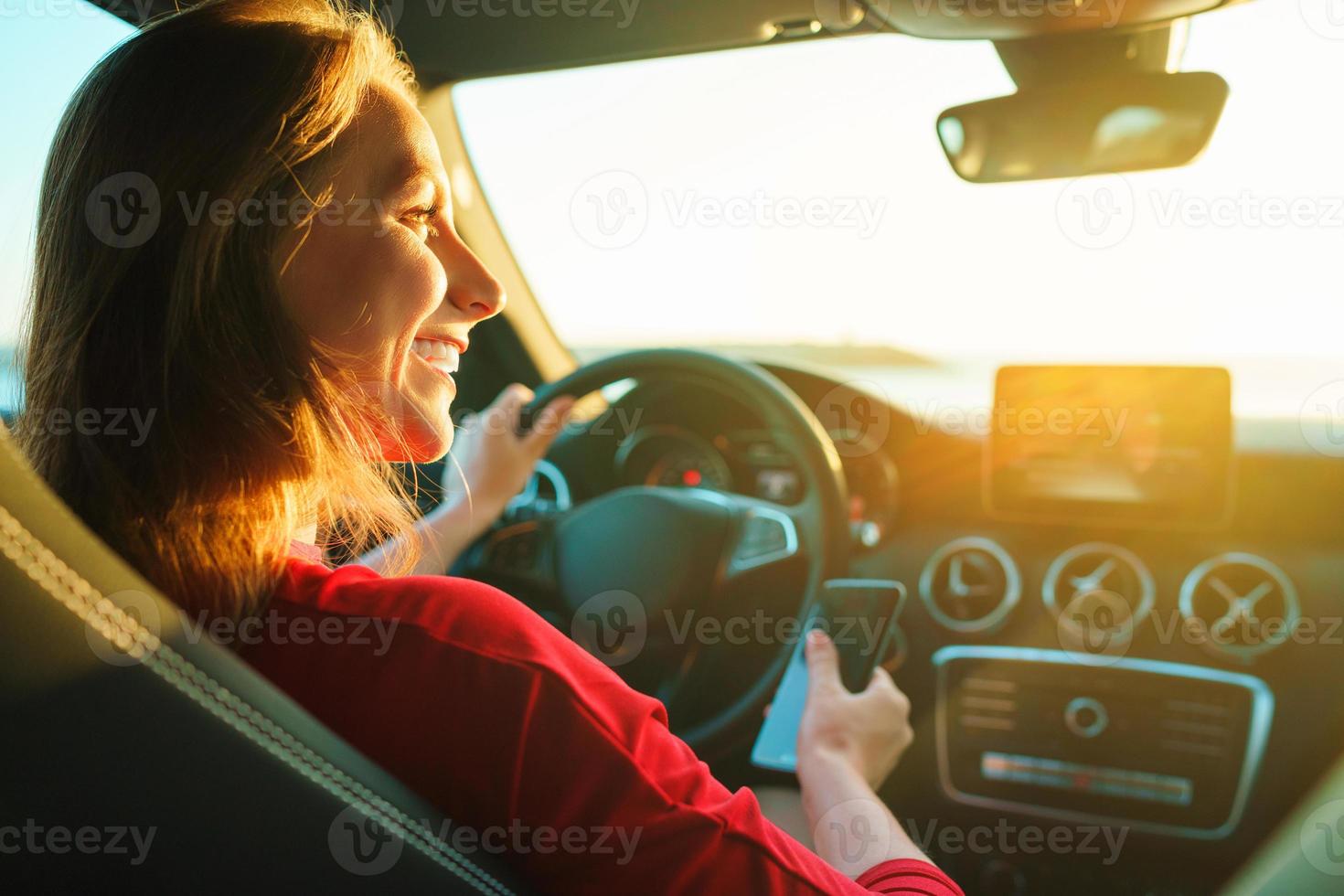 Happy woman uses a smartphone while driving a car photo