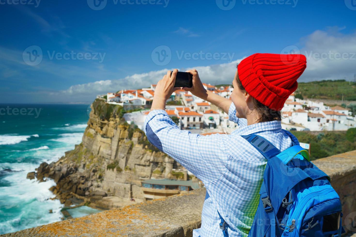 mujer con un mochila hace un foto en el teléfono inteligente de un hermosa panorama de el Oceano costa cerca azenhas hacer mar, portugal