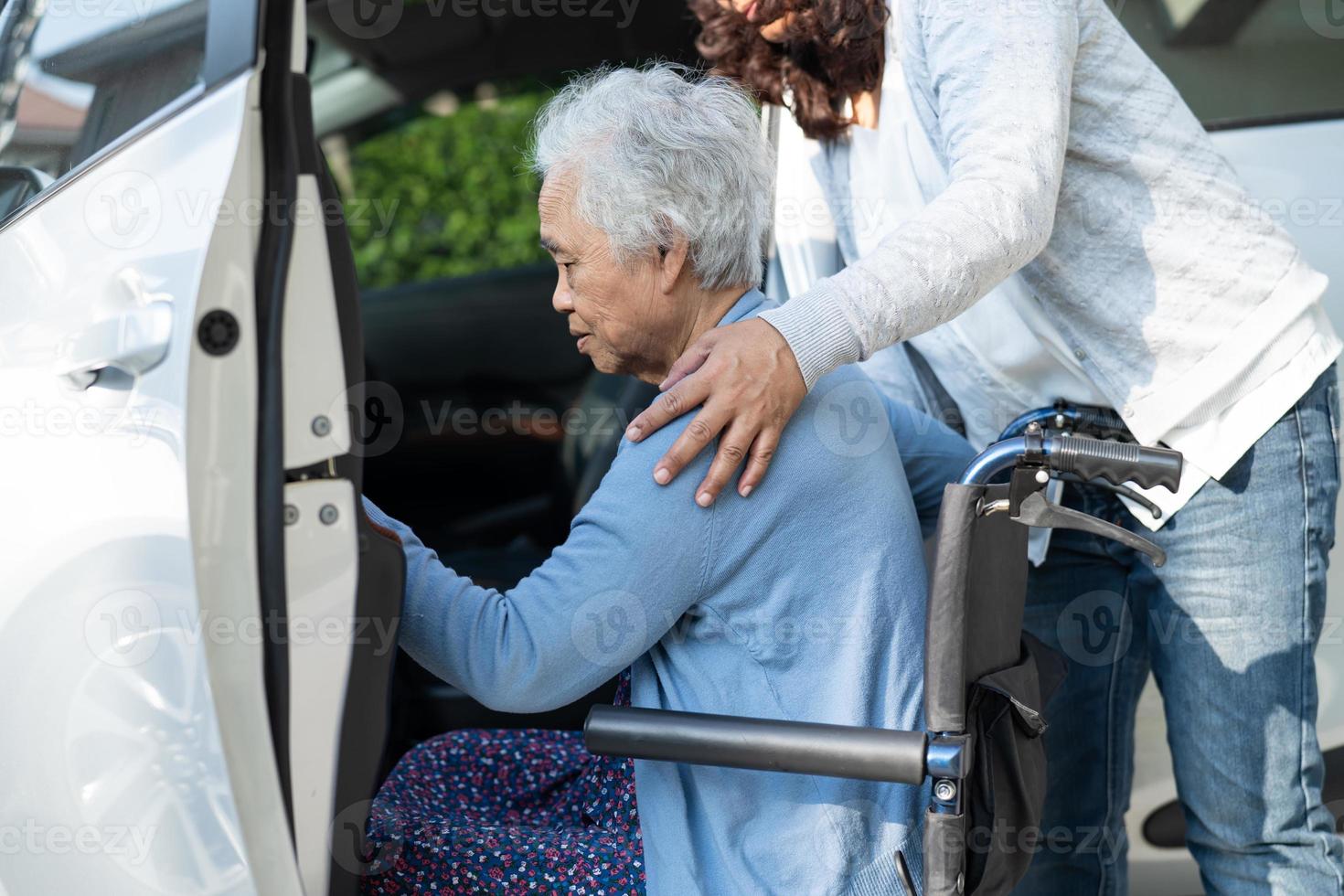 Caregiver help and support asian elderly woman sitting on wheelchair prepare get to her car to travel in holiday. photo
