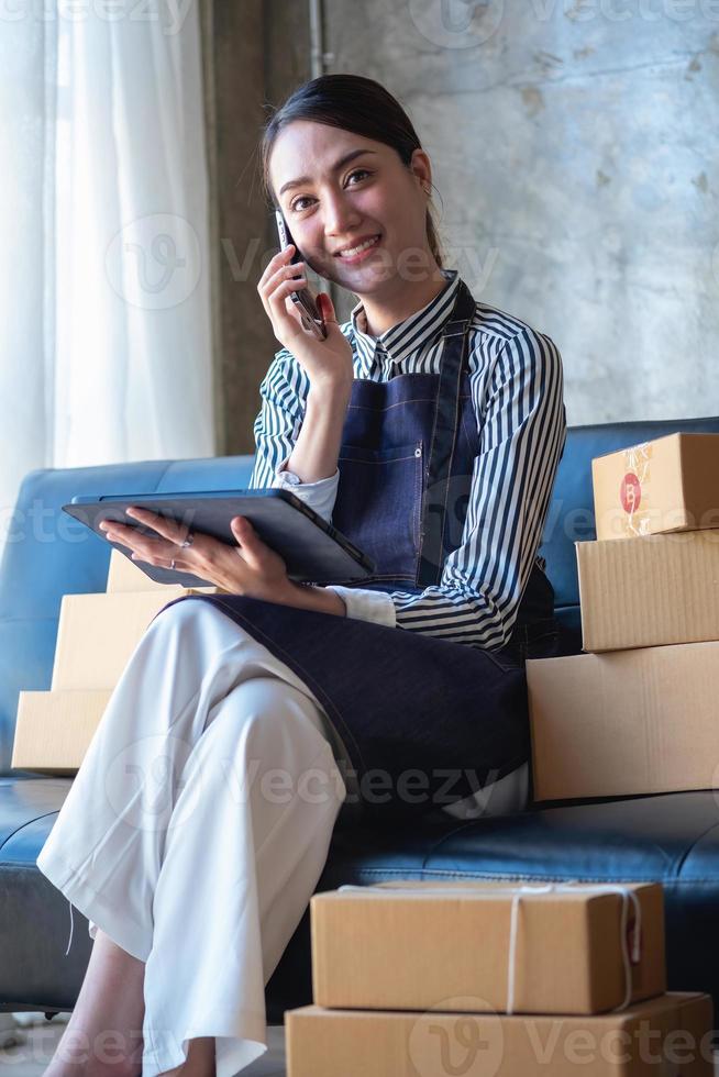 Asian female entrepreneur starting an online sales business using laptops, tablets, and smartphones to place orders and check products inside her own office, SME online concept. photo