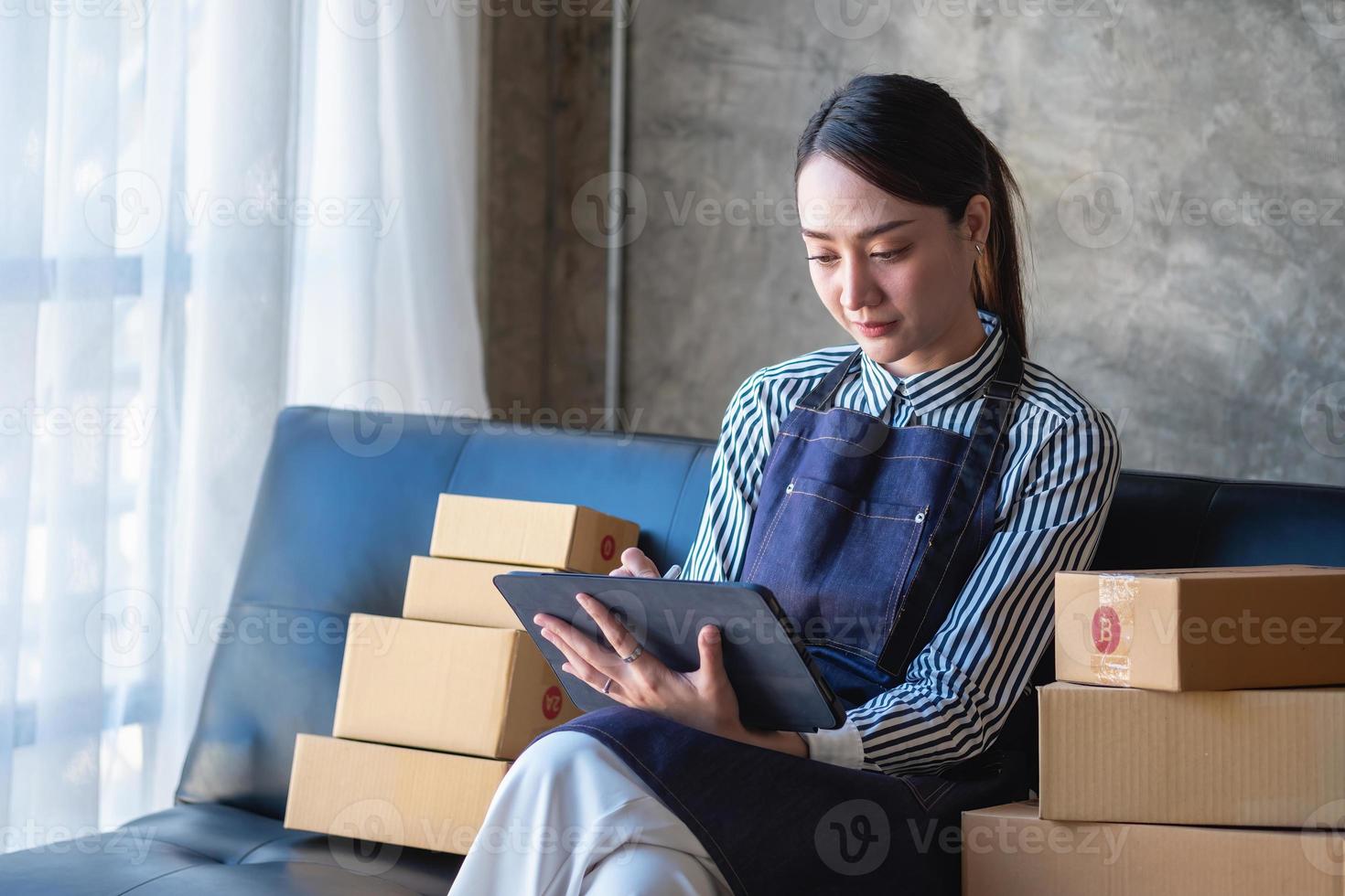 Asian female entrepreneur starting an online sales business using laptops, tablets, and smartphones to place orders and check products inside her own office, SME online concept. photo