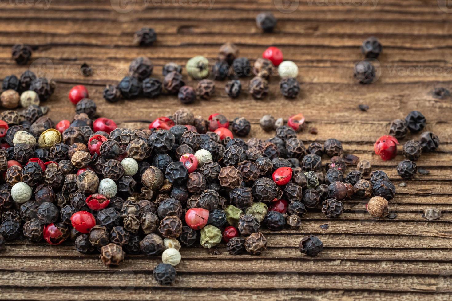 Peppercorns on dark rustic wooden background. Mix of different peppers photo